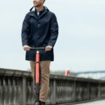 man in blue jacket and orange pants standing on bicycle during daytime